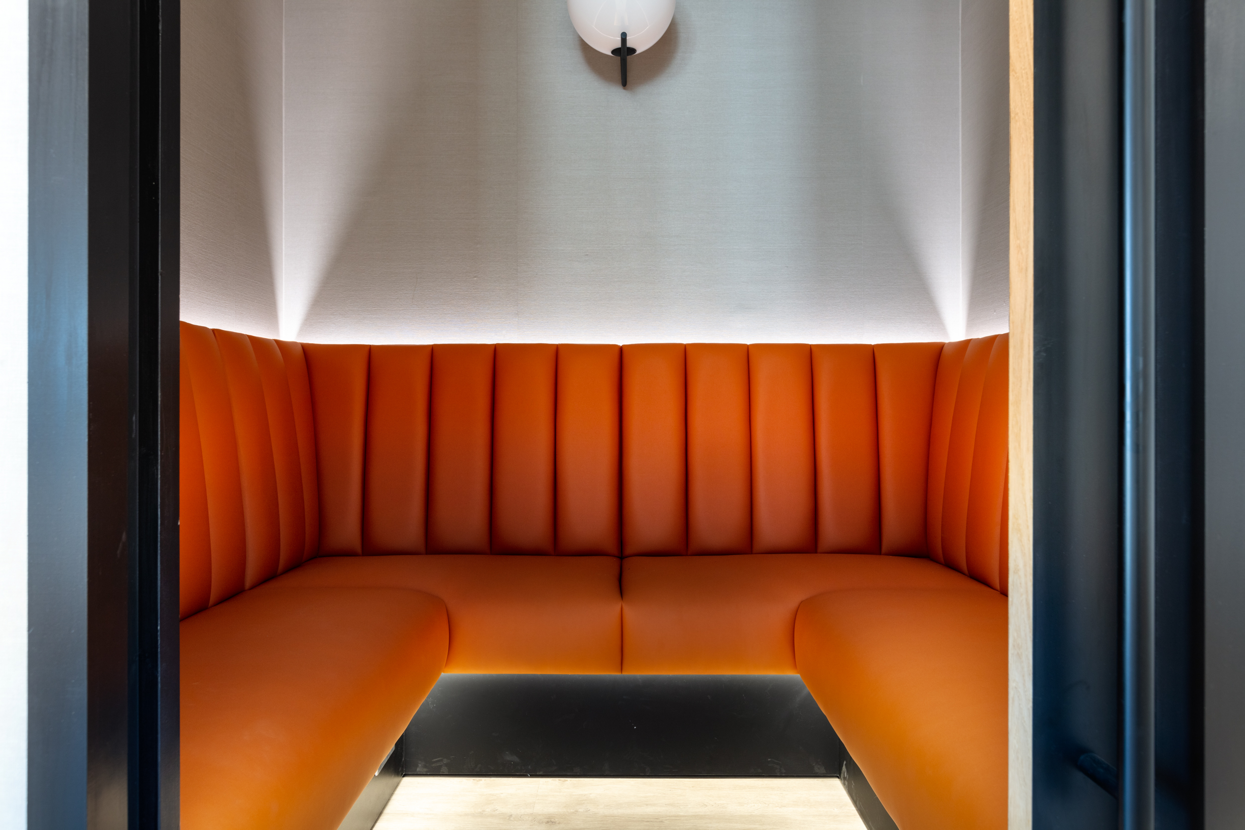 An intimate booth seating area with vibrant orange upholstery, perfect for casual meetings or private work sessions at Ring Central.