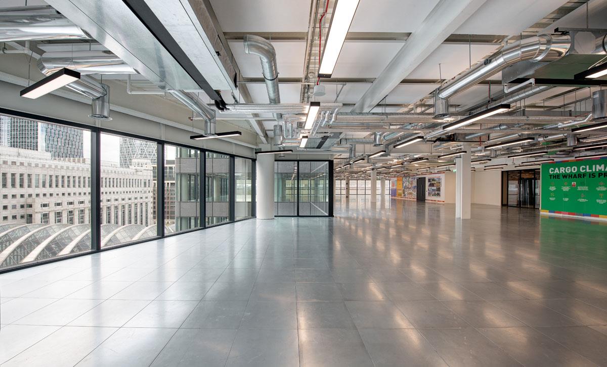Interior of 25 North Colonnade with floor-to-ceiling windows showcasing city views, exposed ceiling ducts, and polished flooring, creating a spacious and modern office environment.