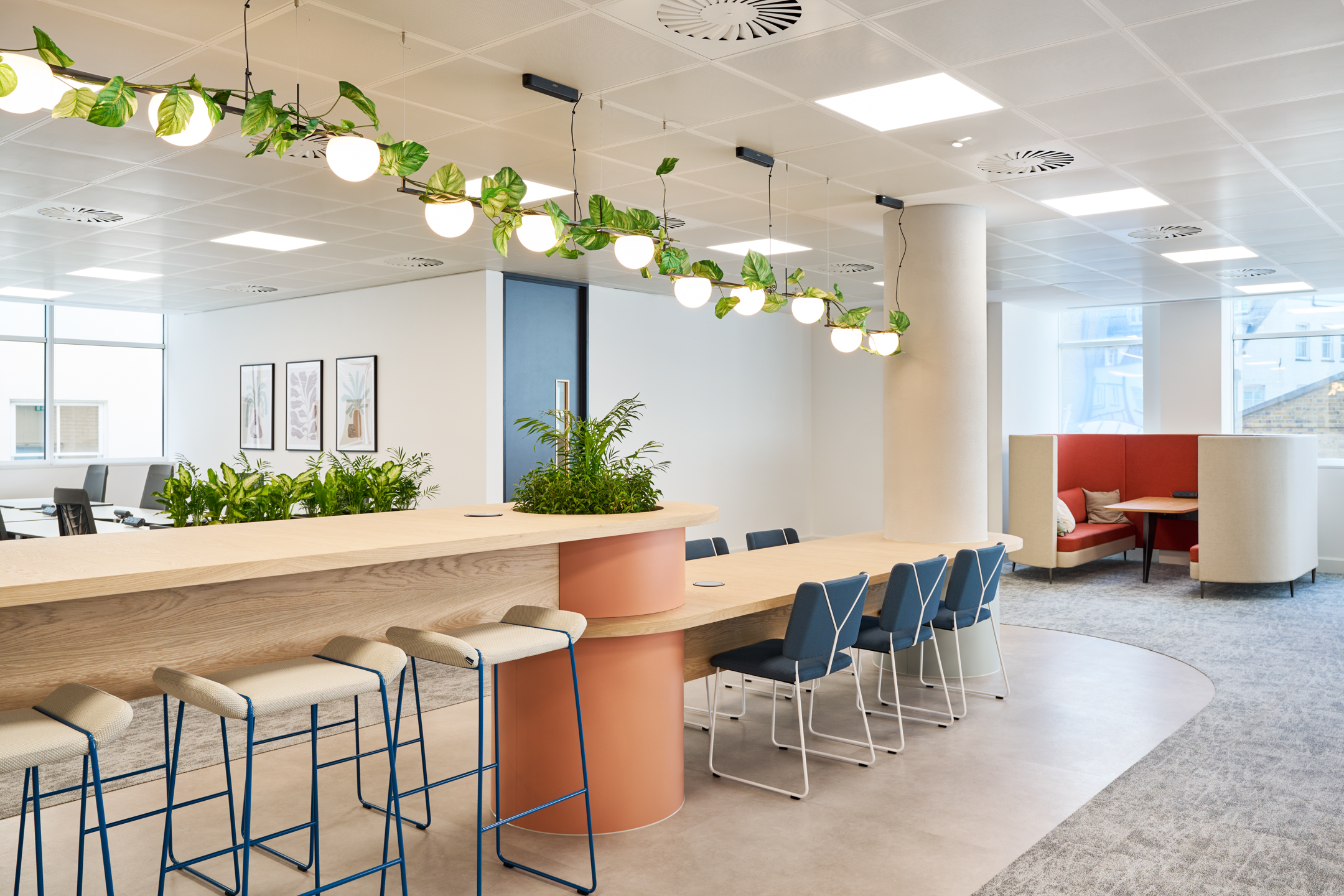 Casual work area at 7 Bishopsgate Level 4, featuring a large wooden worktop with bar stools, under hanging plants and stylish lighting.