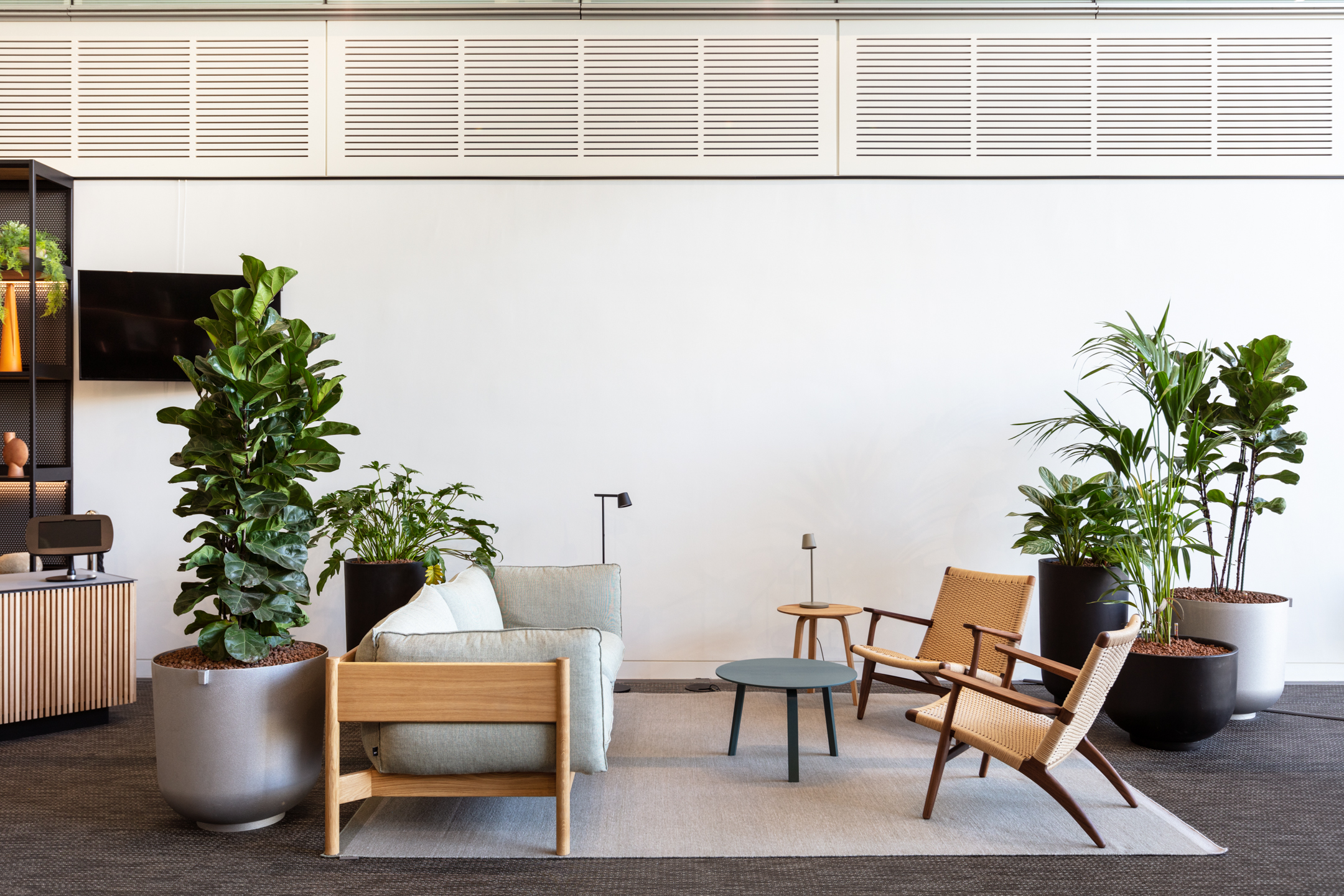 A lounge area with a light sofa, wooden chairs, and an assortment of plants, creating a relaxed and inviting space at Chiswick Business Park Building 9.