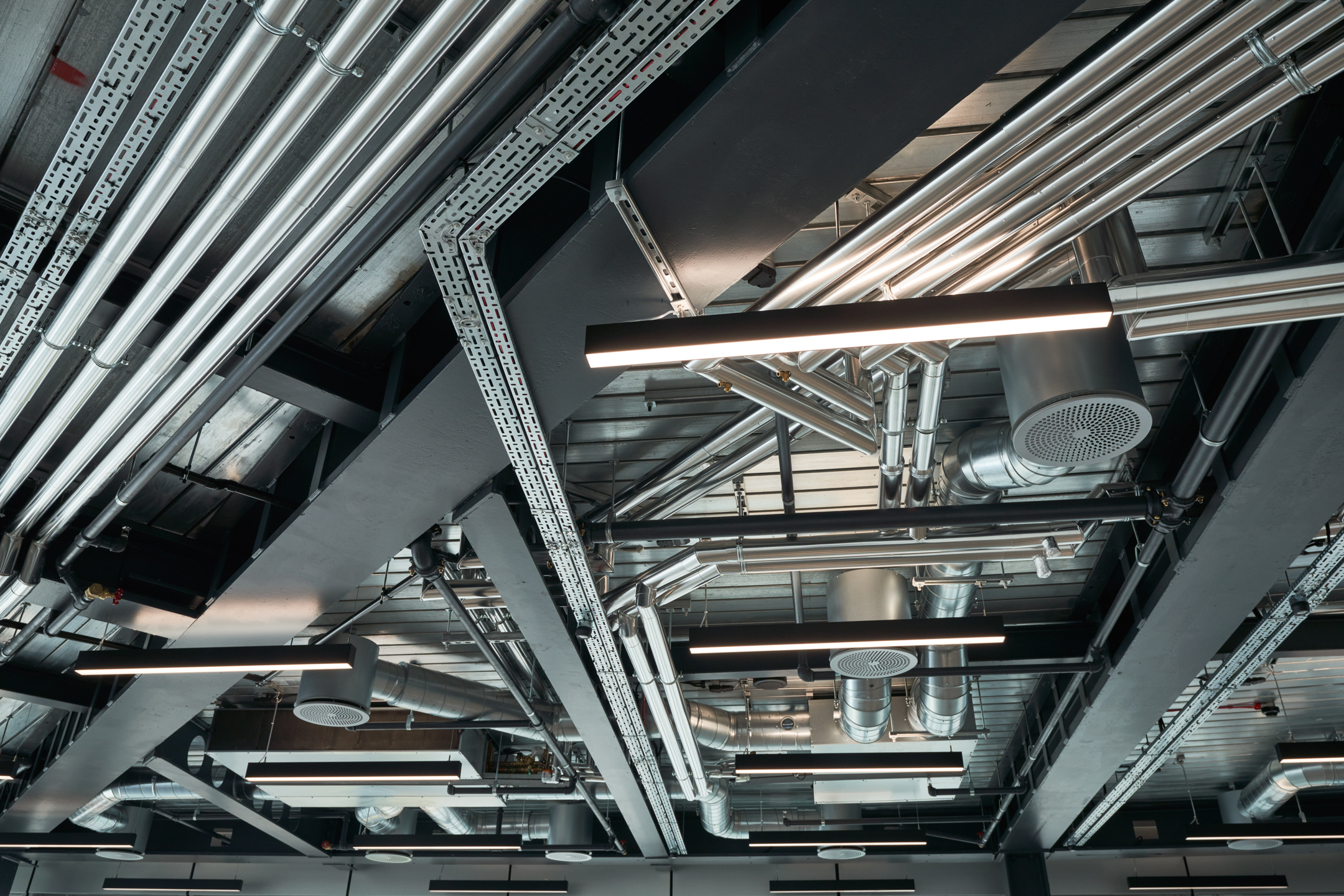 The Point Floor 6 LED bespoke lighting featuring an exposed ceiling with fans, lights and silver construction beams aligned in a geometric pattern