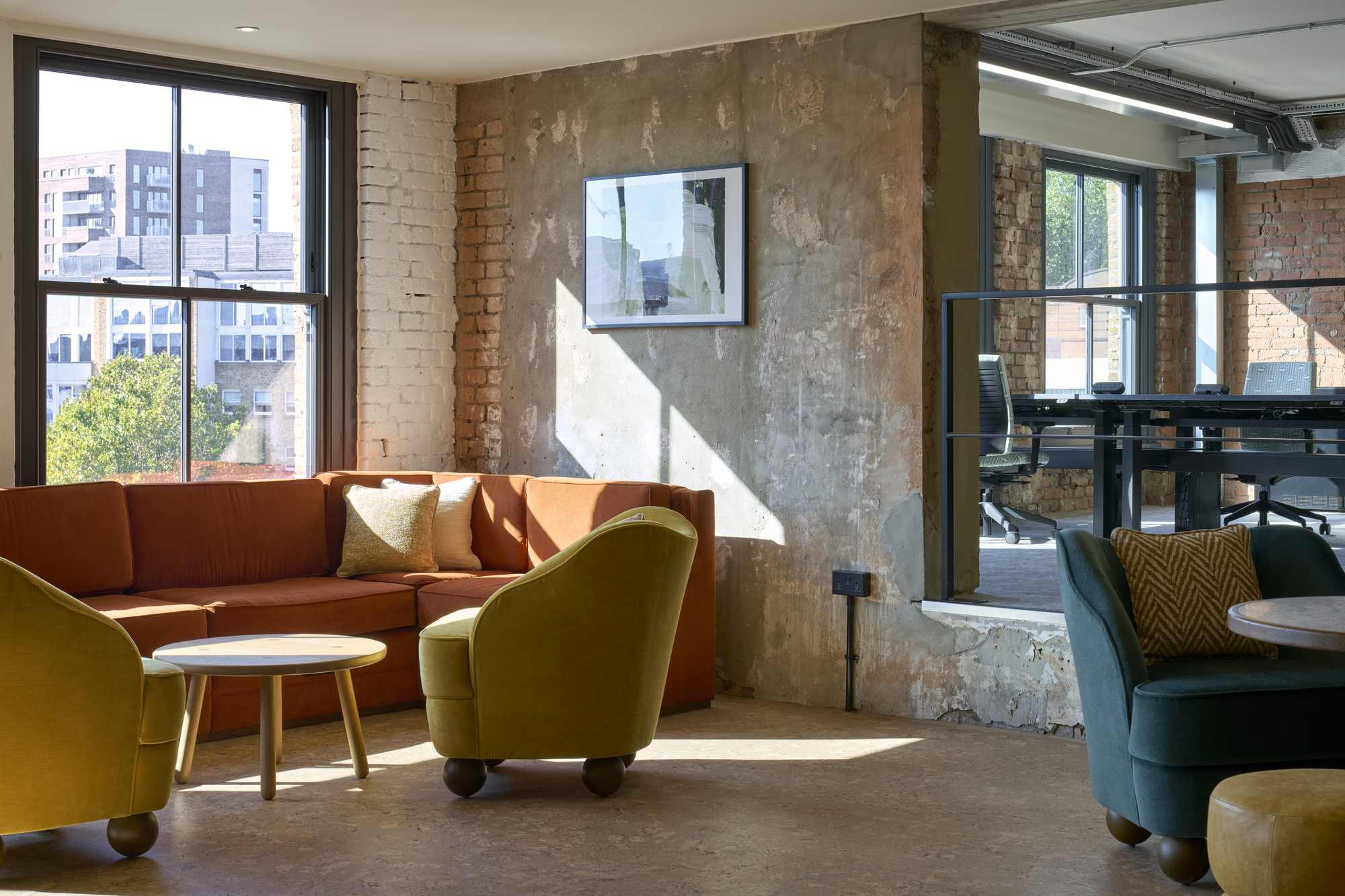 Bright and inviting lounge corner at The Waterman featuring a plush orange sofa, mustard yellow chairs, and a rustic, unfinished wall, creating a relaxed, creative space designed by Ambit.