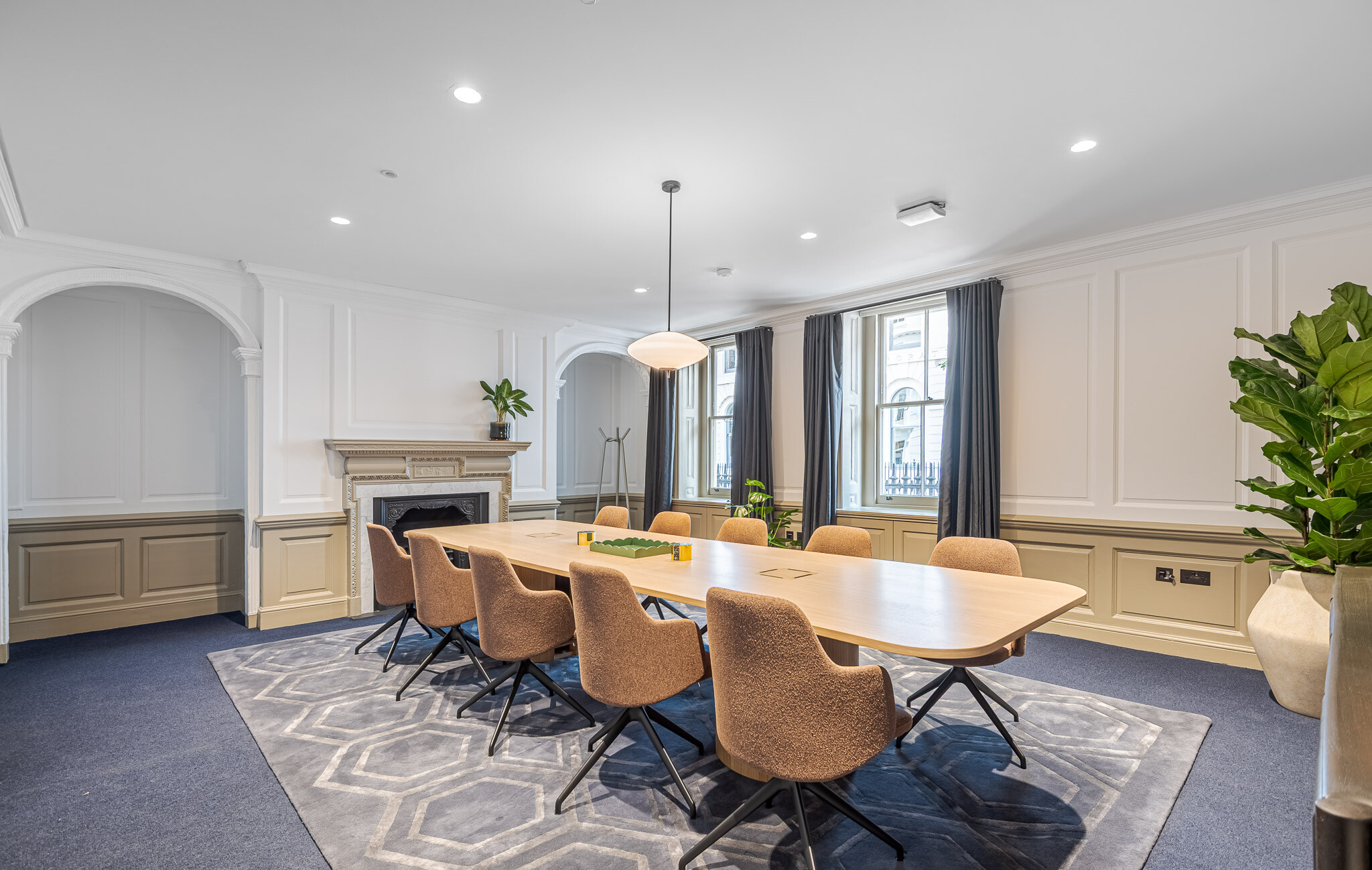 Refurbished meeting room at Bloomsbury House featuring restored heritage fireplace, modern pendant lighting, and a large boardroom table with soft upholstered chairs and original sash windows.