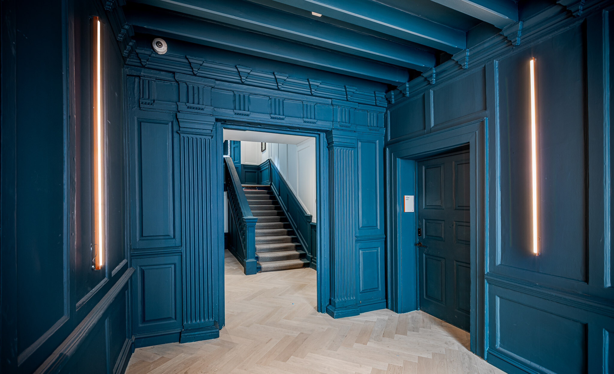 Bold teal entryway at Bloomsbury House showcasing restored timber panelling, integrated vertical lighting, and a view through to the repositioned staircase lined with soft carpeting.