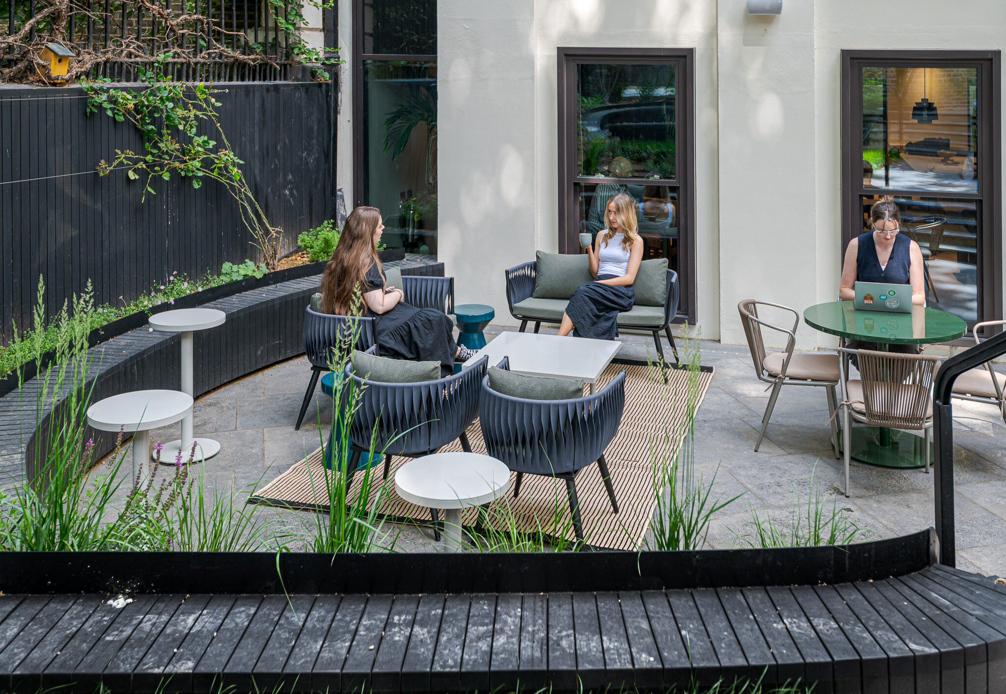 Lively courtyard at Bloomsbury House with curved black timber seating, greenery and outdoor furniture, used by tenants for casual meetings and focused work in a relaxed setting.