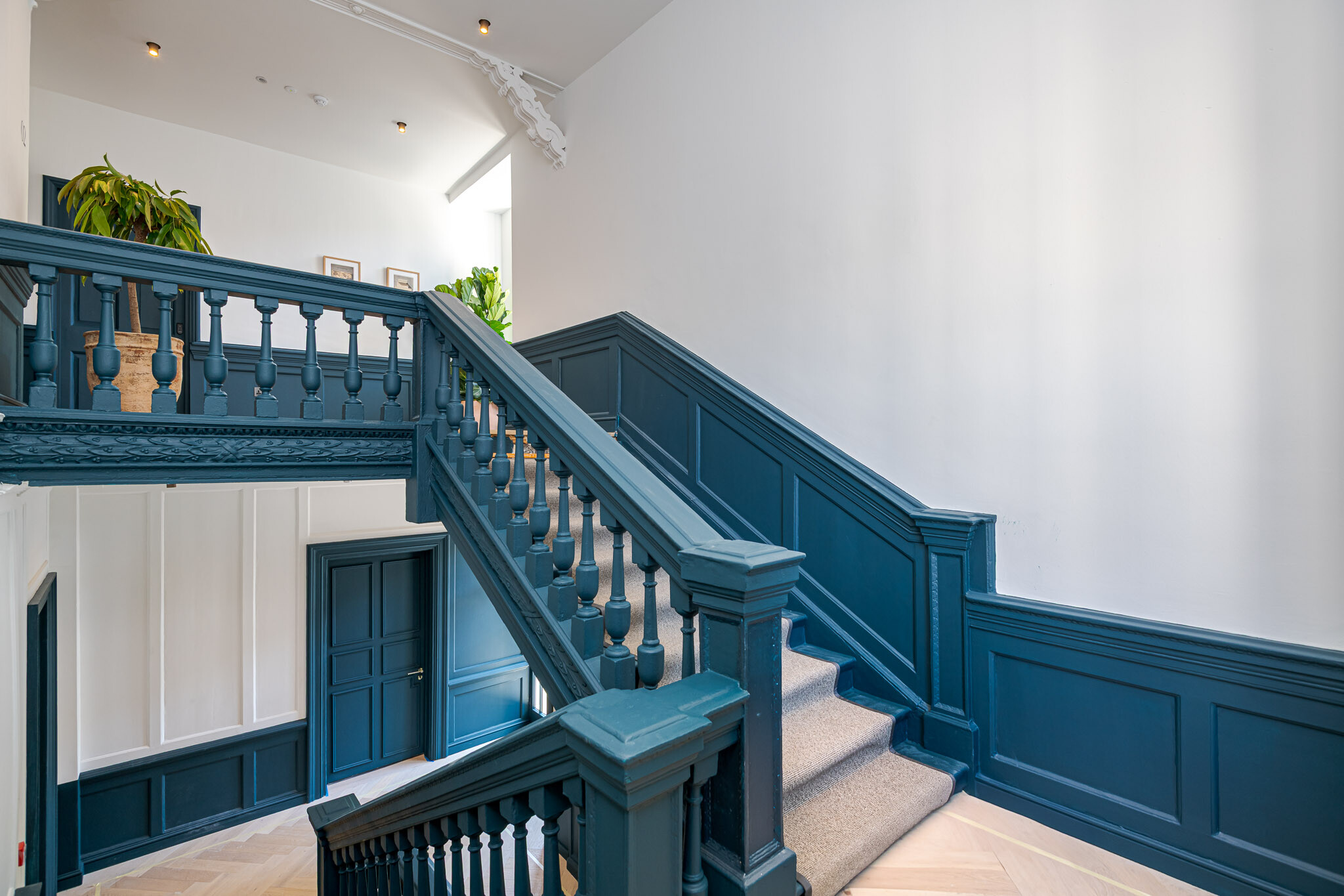 Restored staircase at Bloomsbury House with original balustrades painted in deep blue, natural timber flooring, and soft carpet treads, blending heritage detail with modern finish.