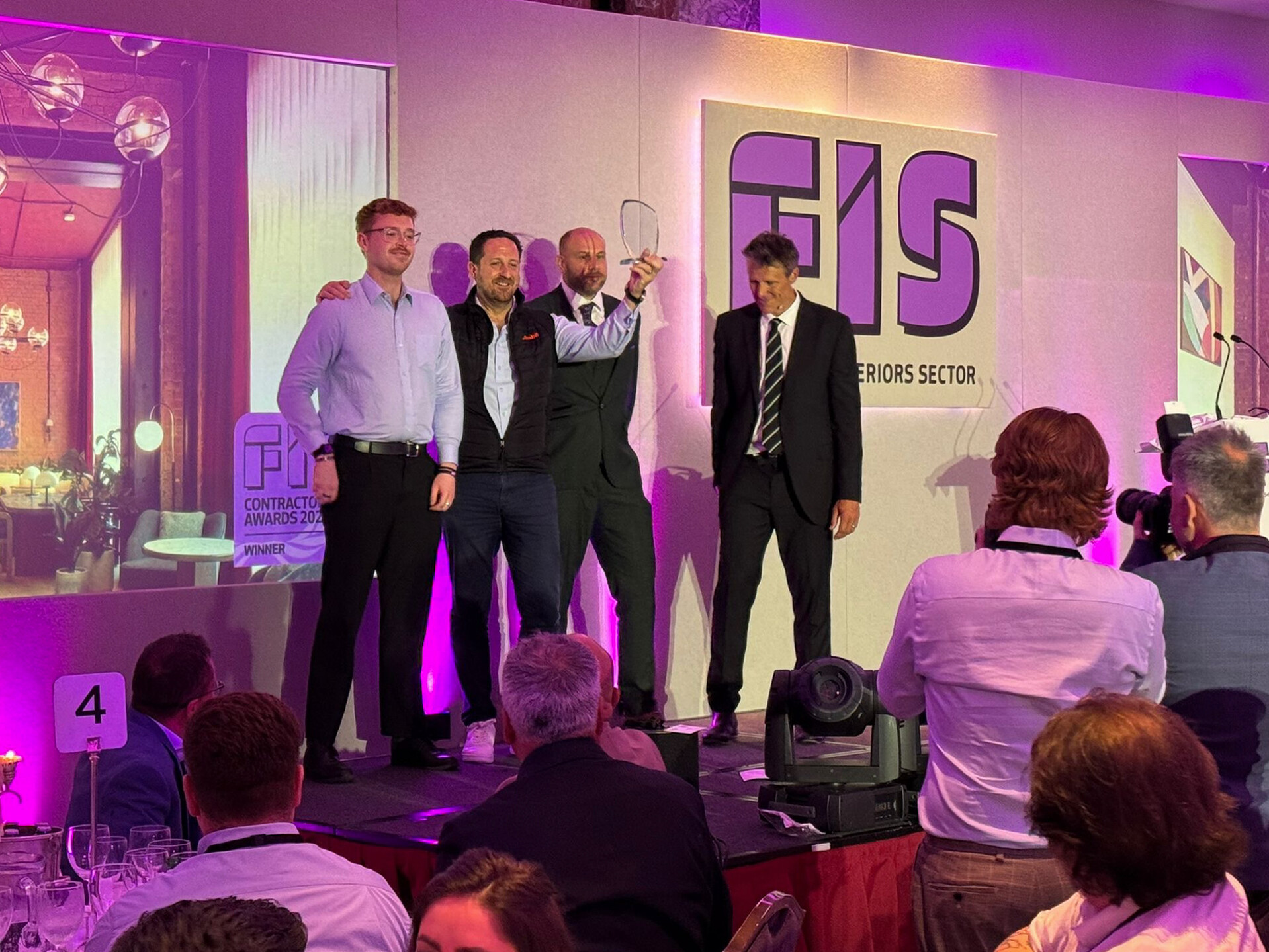 Ambit team on stage receiving the FIS Contractors Award 2025 for Most Sustainable Project at The Waterman, with the trophy held high under purple lighting as photographers capture the moment.