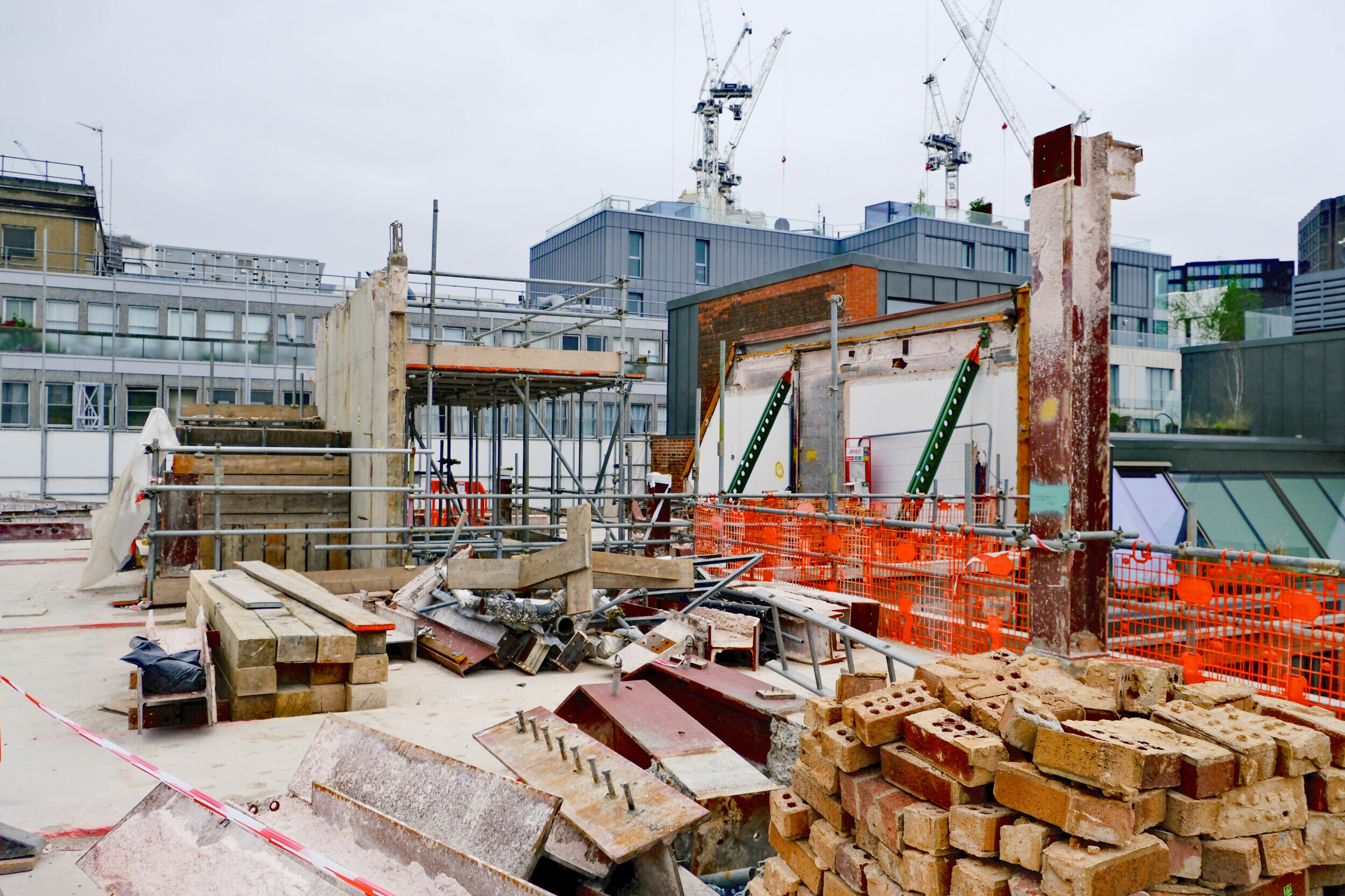 Pile of reclaimed bricks in the foreground of a partially deconstructed building with scaffolding and structural supports, illustrating the Rochester Row Recycling Reused Bricks project.