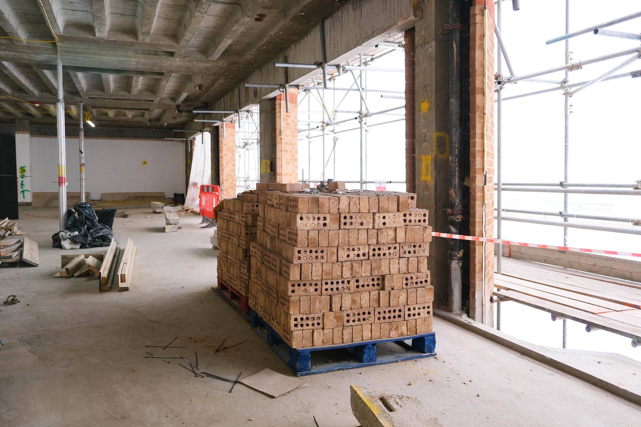 Stack of perforated reclaimed bricks neatly arranged on a pallet inside a partially refurbished building, part of the Rochester Row Recycling Reused Bricks initiative.
