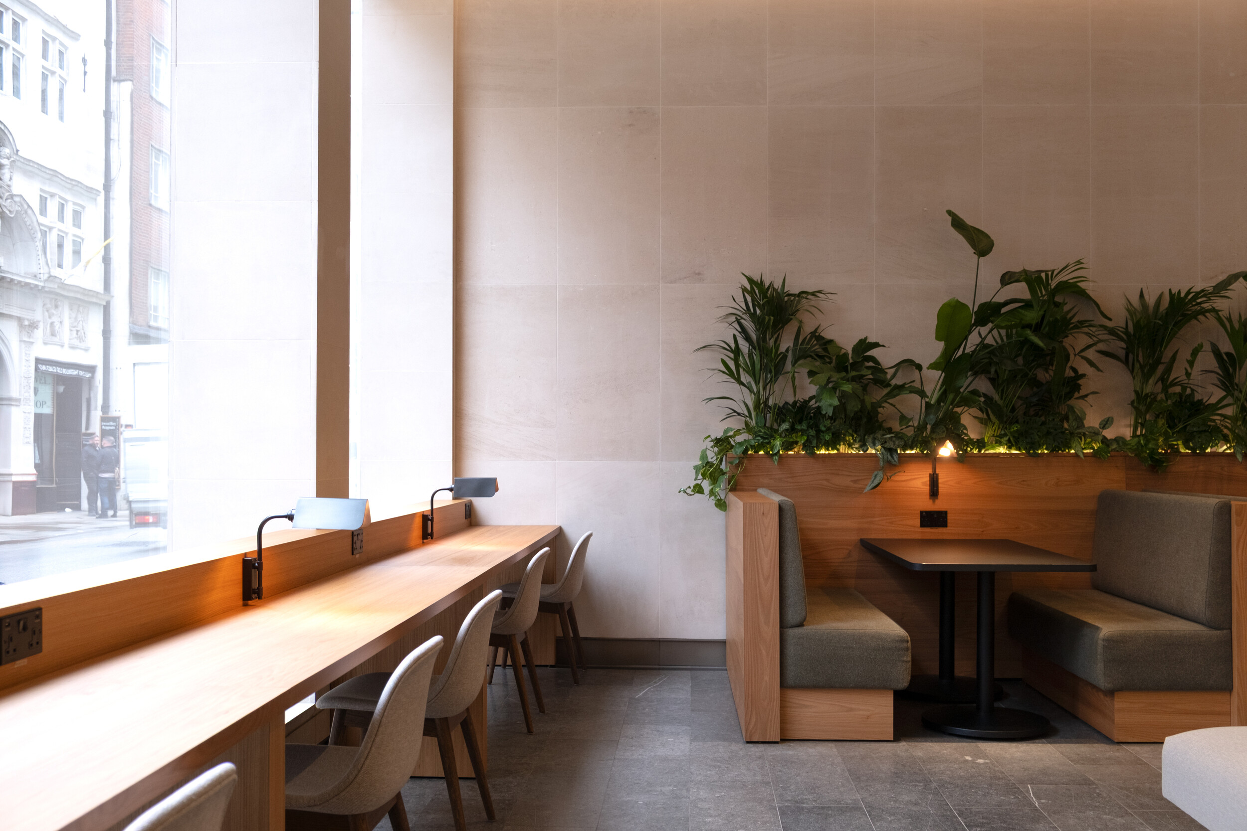 Window-facing desk space and private booth seating at Finsbury Circus House, with built-in planters and soft lighting.