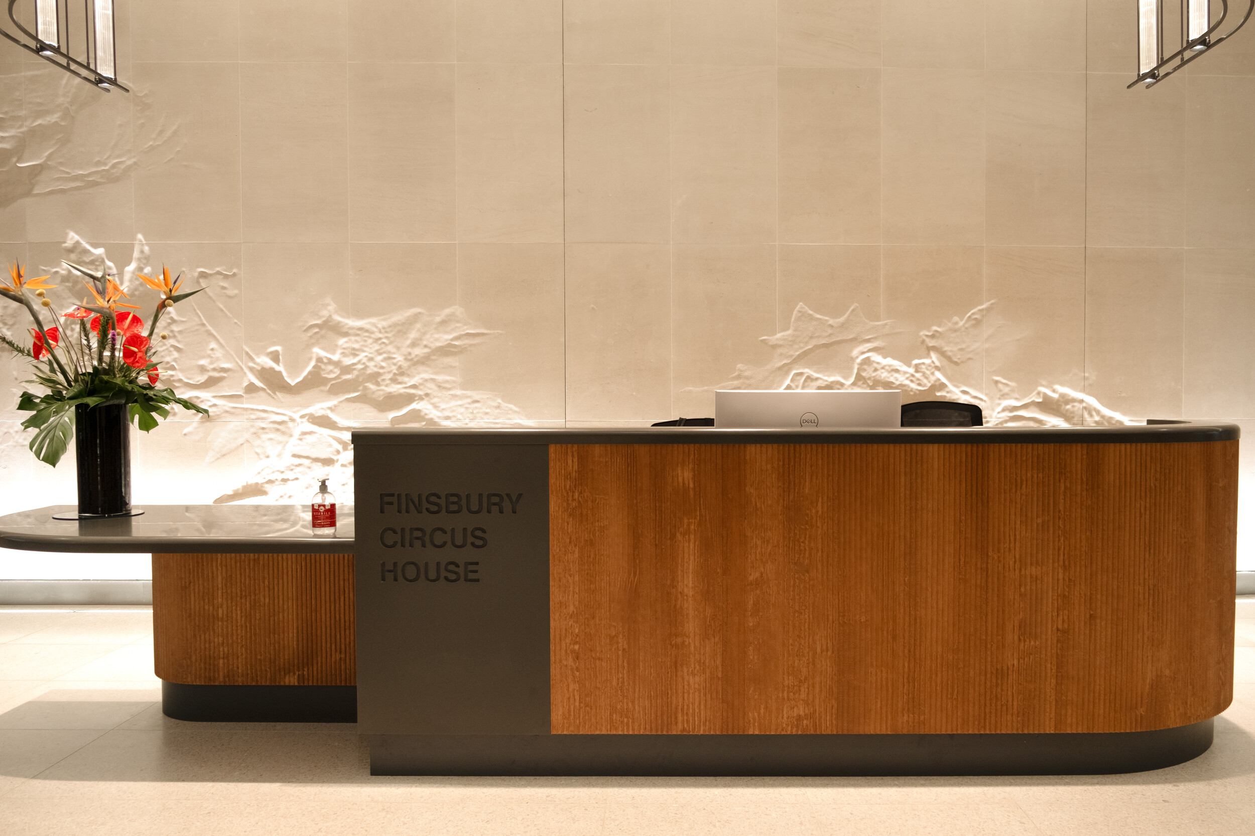 Reception desk at Finsbury Circus House with fluted timber detailing and engraved signage, set against a sculpted feature wall.
