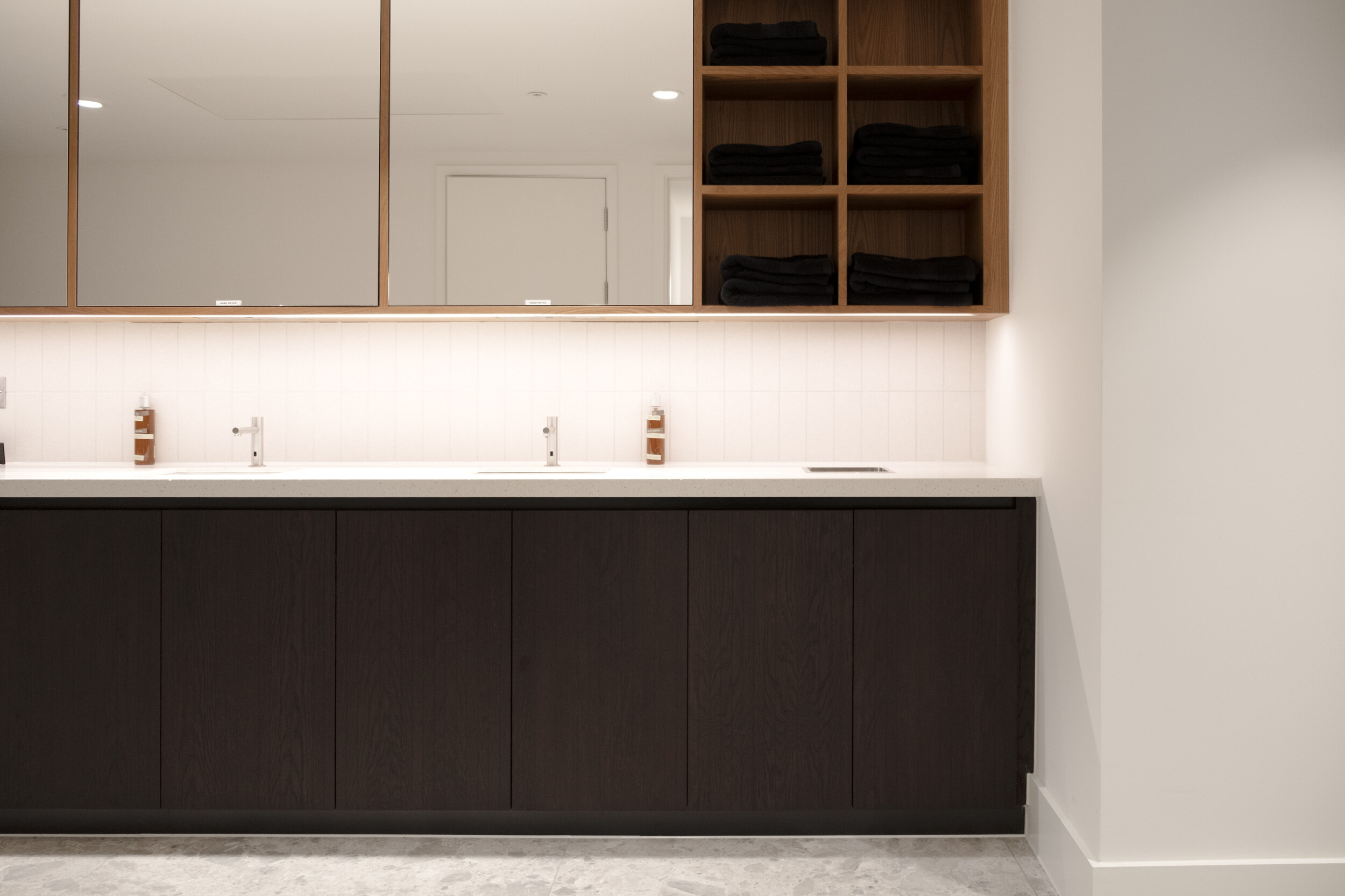 Vanity area within the refurbished lower ground facilities at Finsbury Circus House, featuring dark timber cabinetry, twin basins, and open towel shelving.